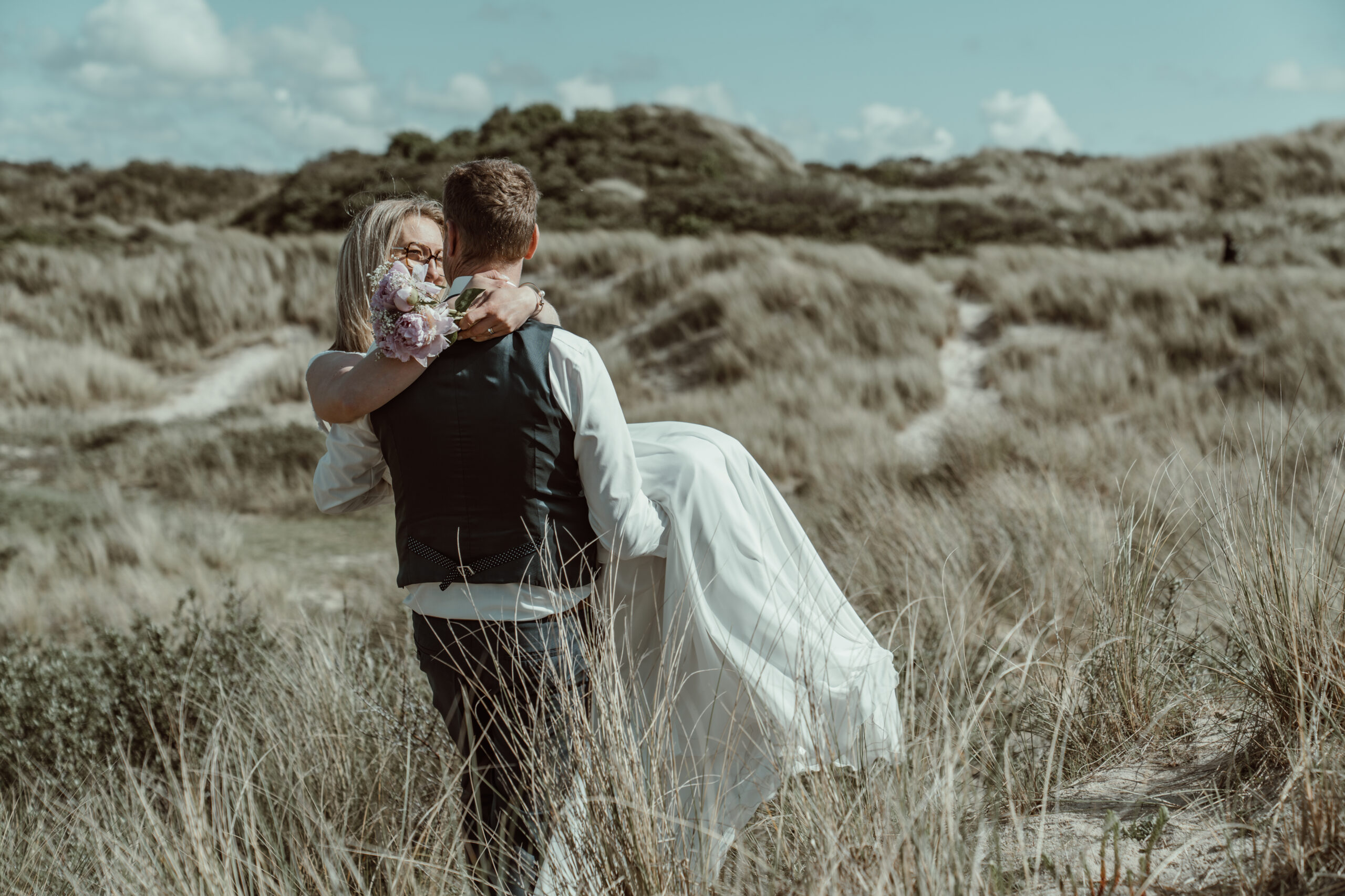 Marié portant sa mariée dans les dunes